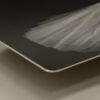A close-up macro shot focusing on the smooth, rounded corner and thin aluminum profile edge of a square 12x12 HD metal art print highlighting the delicate white tulle textures of a ballet tutu against a deep black background.