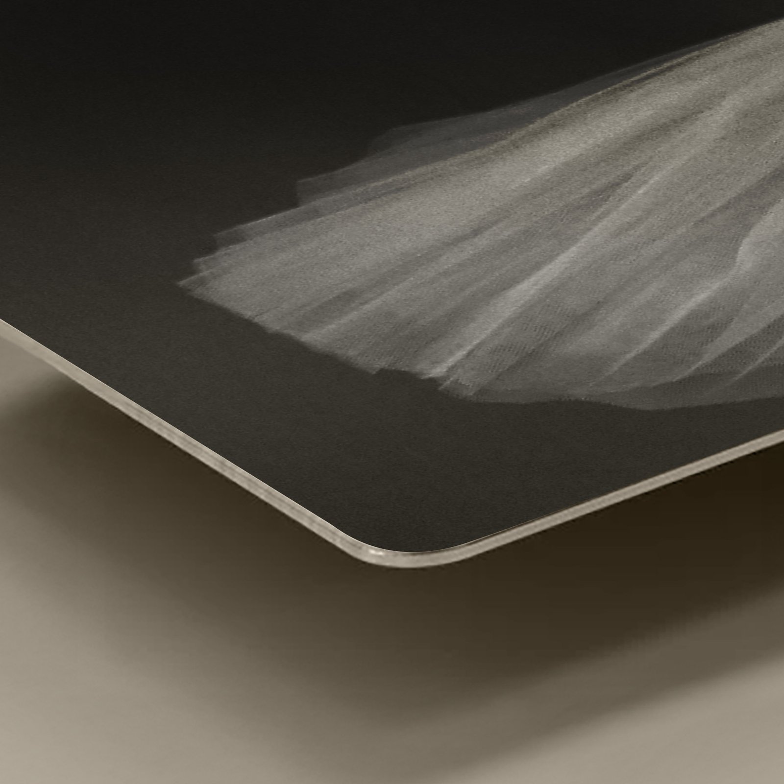 A close-up macro shot focusing on the smooth, rounded corner and thin aluminum profile edge of a square 12x12 HD metal art print highlighting the delicate white tulle textures of a ballet tutu against a deep black background.