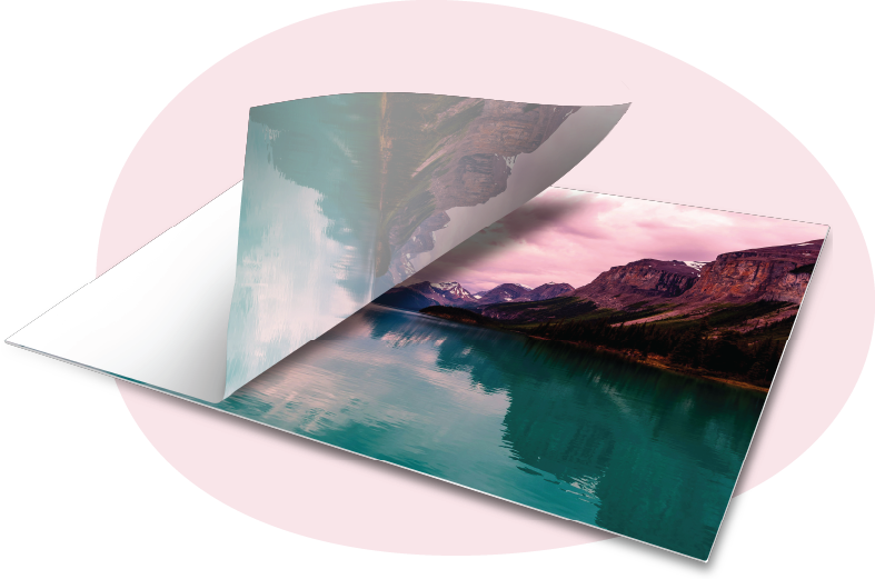 A transfer sheet peeling back to reveal a vibrant landscape print of mountains and a turquoise lake being sublimated onto a surface.