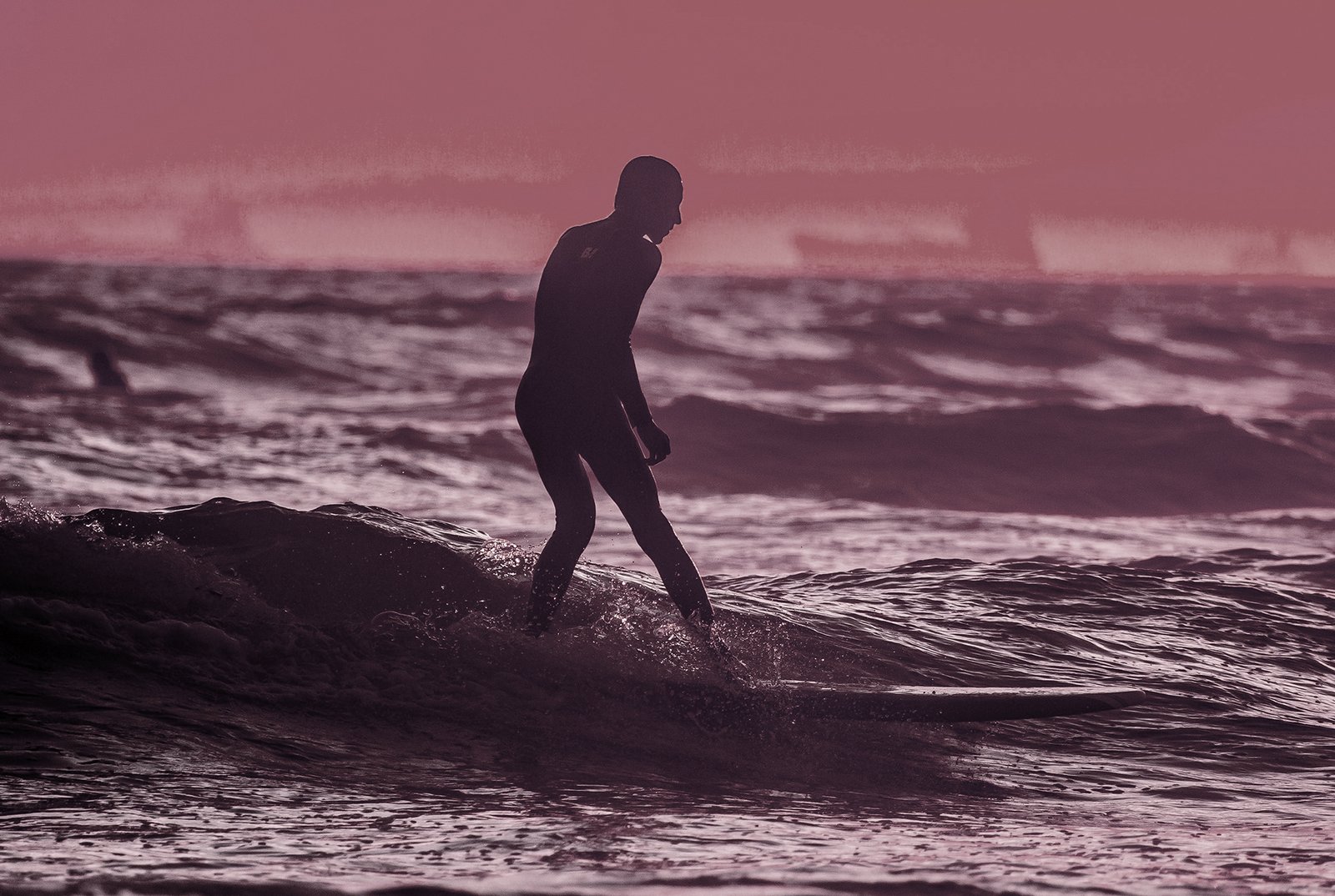 Silhouetted surfer riding an ocean wave in a full wetsuit under a moody pink and purple sunset skyAction sports photograph featuring a surfer silhouetted against dynamic ocean waves at dusk. Toned in muted purple and dusty pink hues, this image is optimized for use as a hero section background, category banner, or full-width promotional graphic for sports, lifestyle, and custom print showcases.