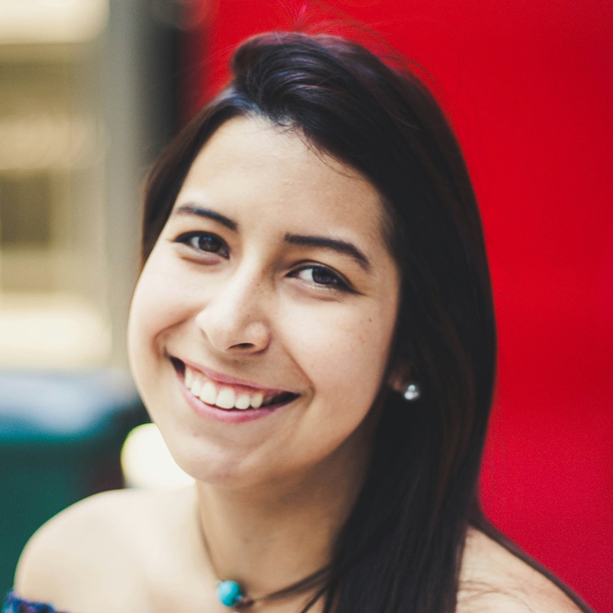 Close-up portrait of a smiling woman with dark hair set against a vibrant red background