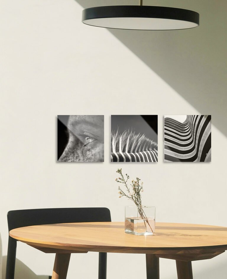 Three square black and white abstract metal photo prints displayed in a row above a wooden dining table