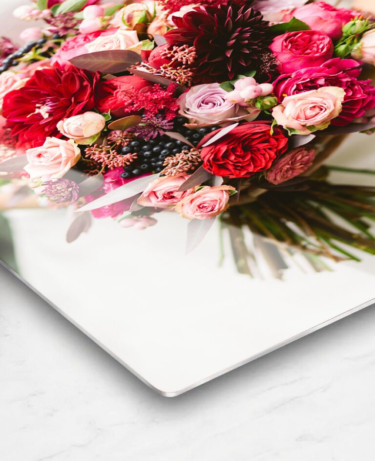 Corner view of a high-gloss metal photo print displaying a vibrant bouquet of pink and red floral arrangement on a white background